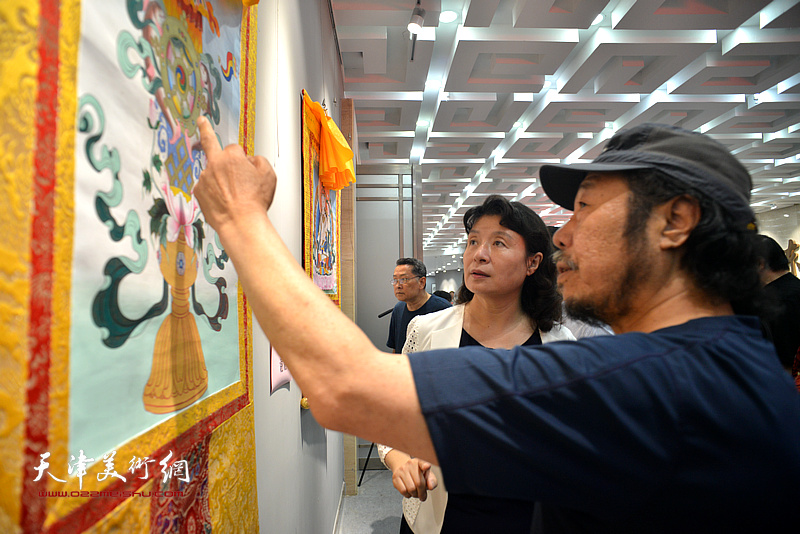 甘南州原美协主席王永胜向万镜明介绍展出的唐卡。
